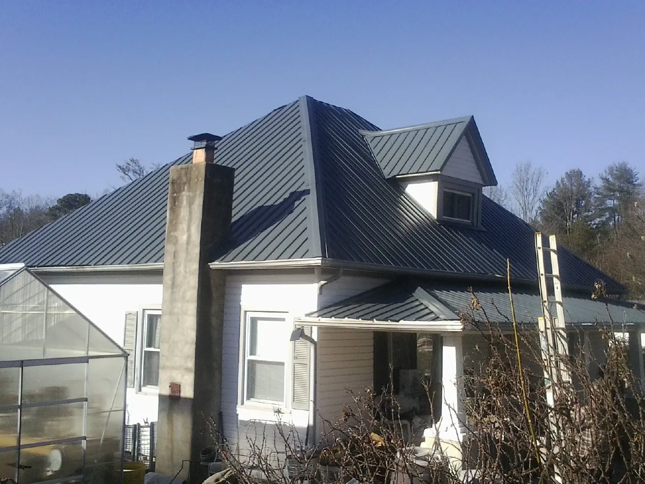 Dark blue standing seam metal roof on a white farmhouse with dormer — Slate & Tile Roof Repair by Roofing Brothers in Gentry