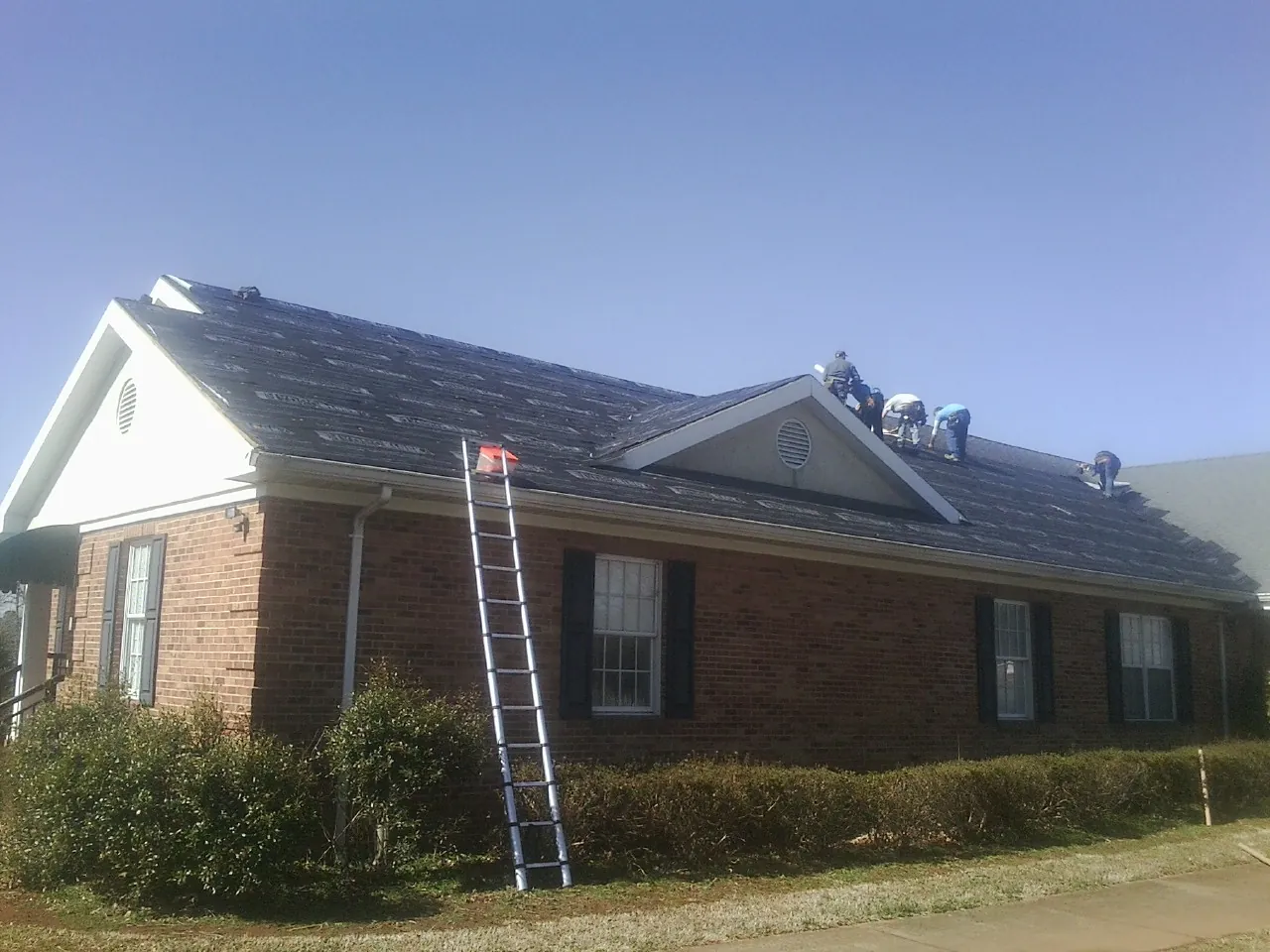 Crew tearing shingles off a brick ranch roof with a ladder set — Metal Roof Repair work by our crew in Gentry