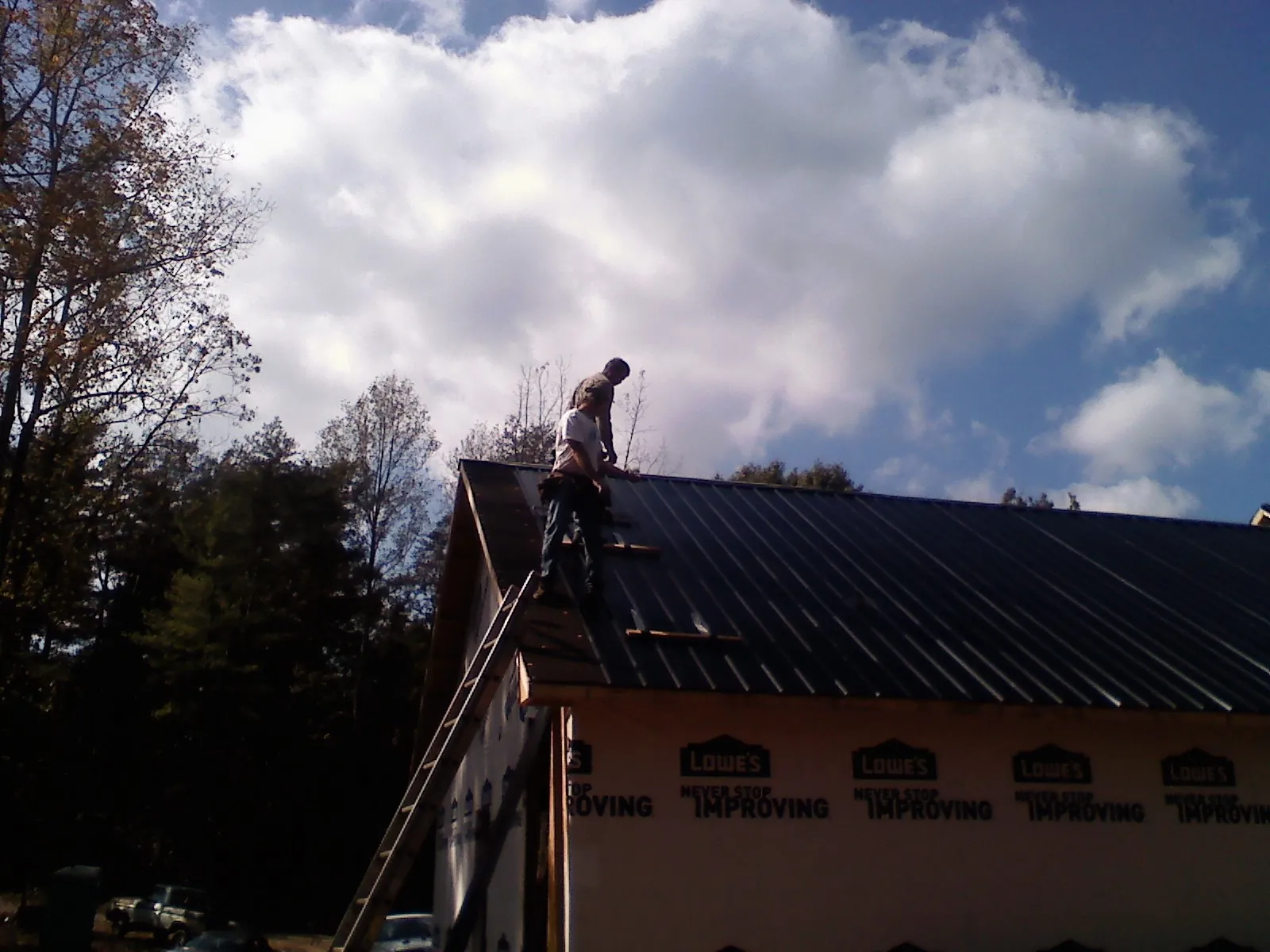 Roofer fastening dark metal panels high against a cloudy sky, from a Roof Inspection job in Gentry