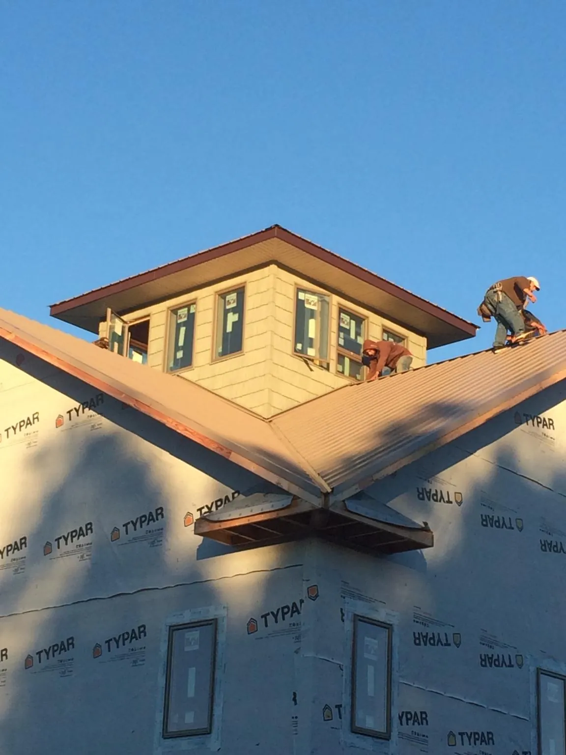 Roofers working around a rooftop cupola on a new metal roof at sunset — Roof Waterproofing in Gentry by Roofing Brothers